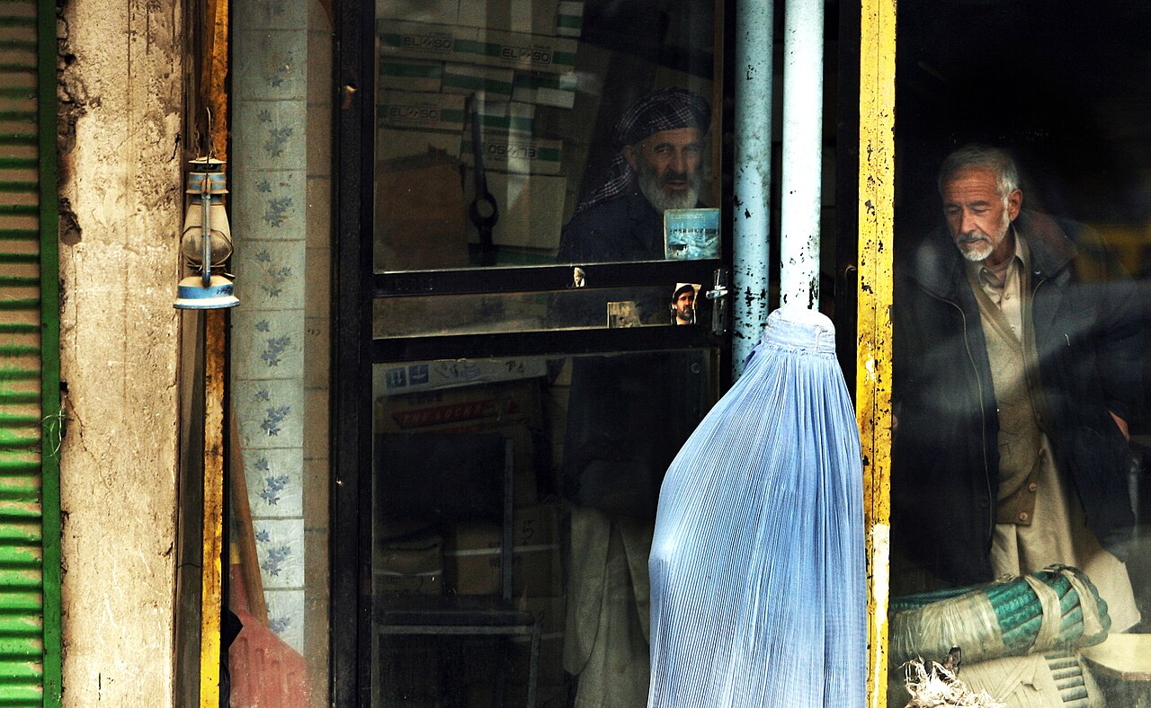 A young Afghan woman in a pale blue burqa at a shop doorway