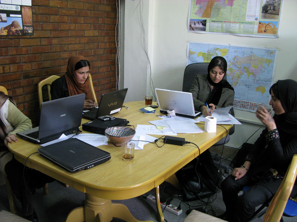 A late-teen Afghan student in an orange headscarf studies at a laptop